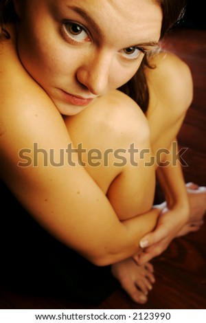 Young woman curled up in a ball, looking at you.
