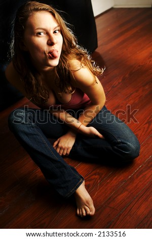 Young woman sitting on floor sticking her tongue out.