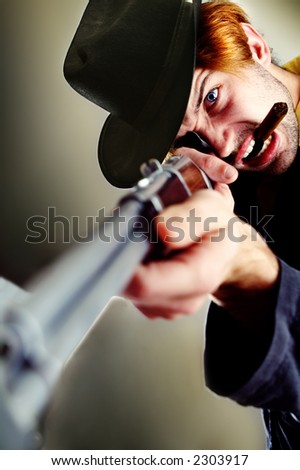 Angry rugged young man with a rifle and cowboy hat. Looks furious at something, probably going to shoot it. Smoking a cigar.