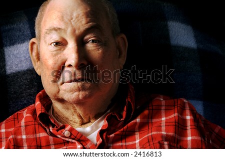 A handsome man in his seventies, wearing a red flannel shirt, smilling.