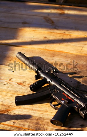 A silenced submachine gun sitting on a table as the sun sets.