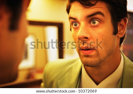 A man in a suit surprised and afraid at what he has found in the mirror.