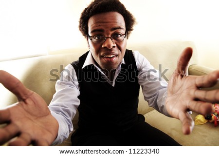 A black man on a couch reaching out for a hug, or asking a question.