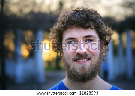 Young man with a beard smiling at the park.
