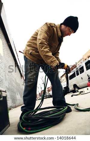 An electrician on a film set wrapping up bates cable for a move.