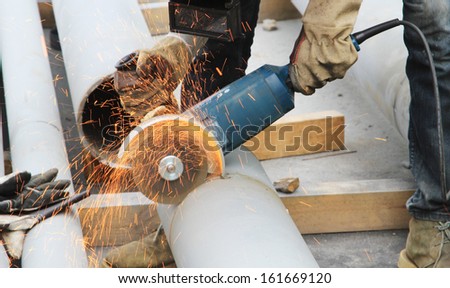 Worker cut steel pipe by grinder, working place background.