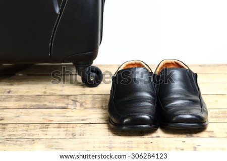 Black leather shoes and  luggage travel bag on the wooden table