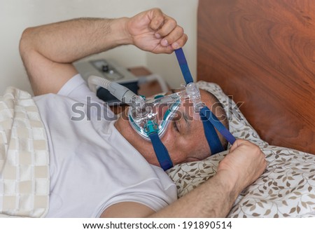 Man suffering from sleep apnea sleeping wearing and adjusting the CPAP mask.