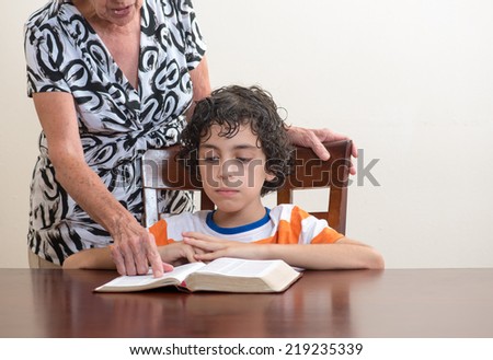 Grandmother teaching the Holy Bible to her grandson. Hispanic family studying the word of God in their daily Christian devotional. Reverence to God learning from His word.