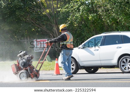 TORONTO,CANADA-OCTOBER 11, 2014: Man repairing a busy Toronto street during the day and using equipment. Toronto city is the Capital of Ontario and a the Financial Core of Canada