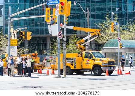 TORONTO,CANADA-MAY 23,2015: Guild of Electric workers: Construction workers in lift bucket truck working on Queen's Park lights behind people on the sidewalk infant of a commercial building
