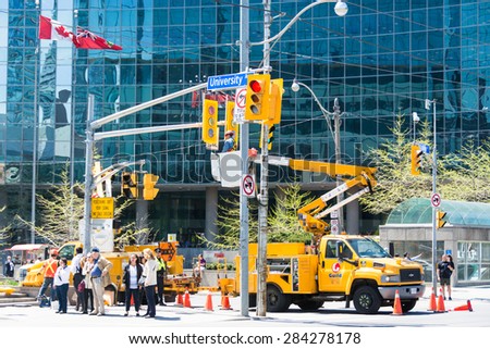 TORONTO,CANADA-MAY 23,2015: Guild of Electric workers: Construction workers in lift bucket truck working on Queen\'s Park lights behind people on the sidewalk infant of a commercial building