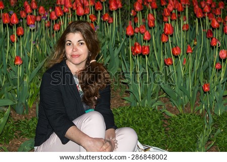 Night Portrait in tulip garden: Beautiful Hispanic woman sitting on the grass with flowering tulips