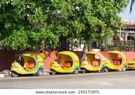 HAVANA,CUBA-AUGUST 12,2014: Coco taxi a tourist affordable transportation: Parked yellow and green motor tricycles in a row next to the curb on an empty street