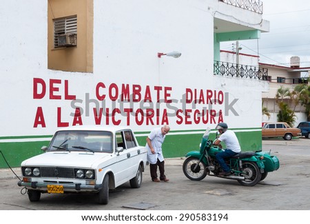 SANTA CLARA,CUBA-JULY 14,2014:  Cuban images: A doctor inflating Lada tires or wheels. Two men see the old soviet car and motorcycles in the streets of the Cuban city.