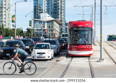 TORONTO,CANADA-JUNE 15,2015: Cyclist passing by a traffic junction as cars and a tram wait for the signal to turn green. Vehicles stopped at the traffic signals awaiting their turn.