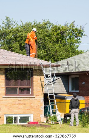TORONTO,CANADA-JULY 25,2015: Workers fixing electric wires to a pole on top of a house.