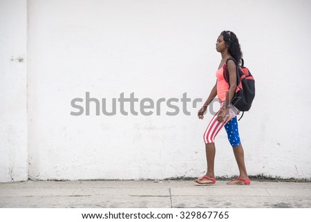 HAVANA,CUBA-SEPTEMBER 20,2015:Everyday life in Cuba: Young lady wearing a USA flag pants walks on a street along a white colored wall.