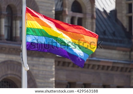 Toronto Pride Month: Rainbow flag waving againt the Old City Hall background. Toronto City successfully launches the first Pride Month in Canada. The event took place on top of the new City Hall