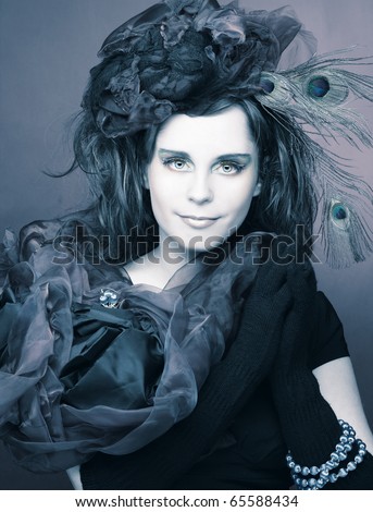 Portrait of young lady in hat with peacock feathers and in blue beads on her hand.