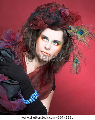 Portrait of young lady in hat with peacock feathers anf in blue beads on her hand.