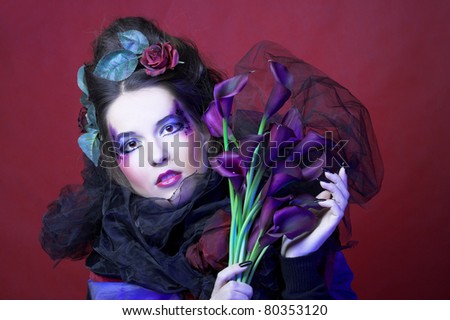 Romantic portrait oj young woman in creative image and with dark flowers in her hands