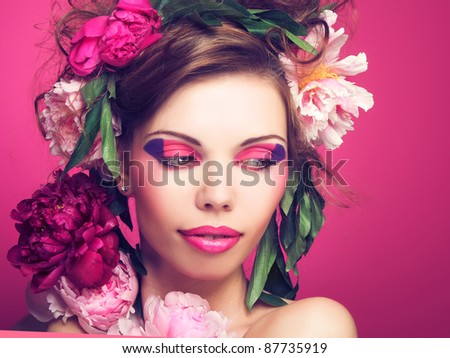 Portrait of young charming woman with  flowers in her hair on the pink background