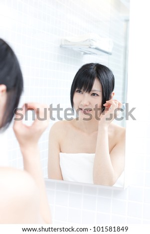 young woman applies makeup in front of a bathroom mirror