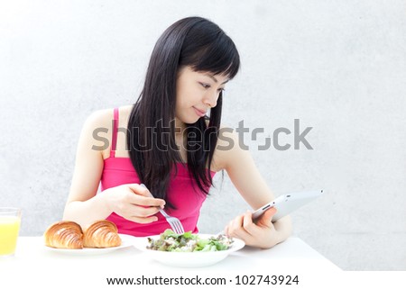 beautiful young girl eating breakfast and using tablet computer.