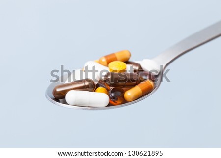 medical pills on spoon, against pale blue background