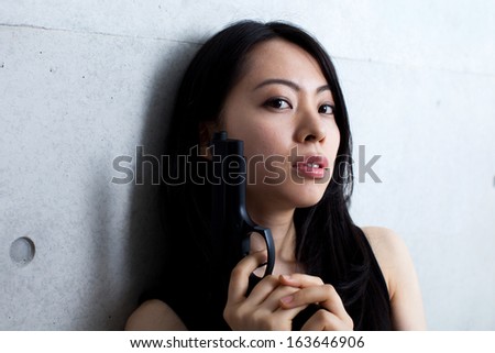 beautiful woman with gun against concrete wall