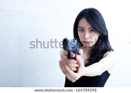 beautiful Asian woman with gun against concrete wall