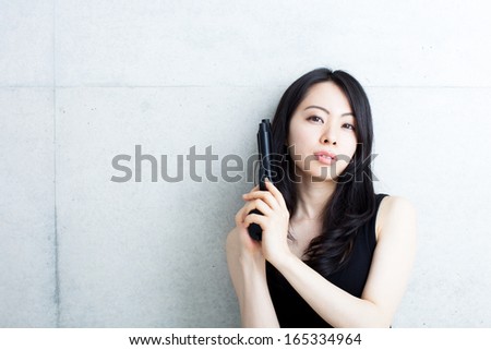 beautiful woman with gun against concrete wall