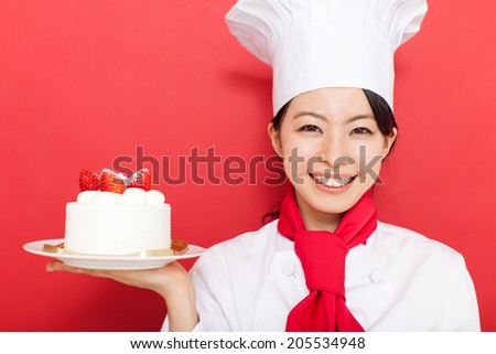 beautiful young cook woman holding a whole cake against red background