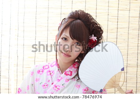 Young girl in Japanese kimono fanning herself by the window