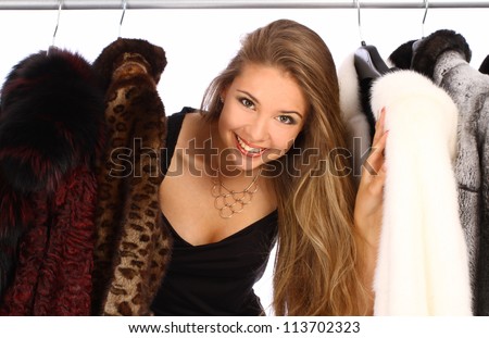 Attractive young woman in her dressing room with a fur coats on the hanger