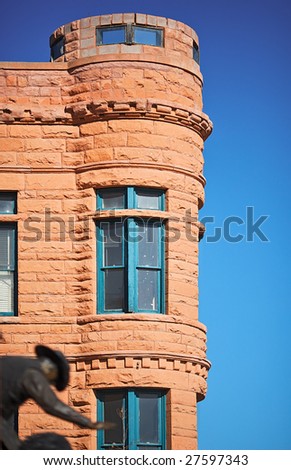 Old western building with a turret. Blue sky in background and cowboy bull rider in the foreground.