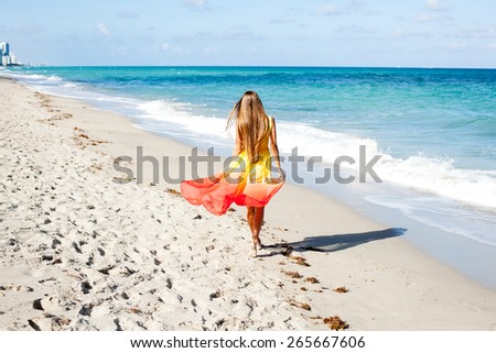 attractive young woman in pretty dress walking on the beach on her amazing summer vacation