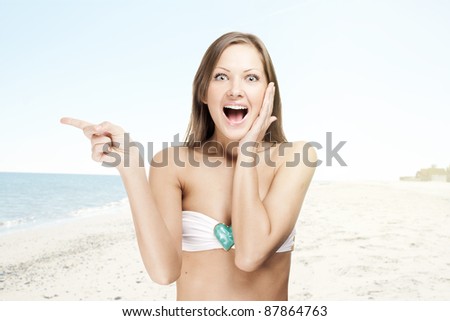 young attractive happy girl in a swimsuit , on the beach , pointing to the right edge