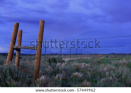 Barbed wire fence with wooden posts in desert plain at dusk