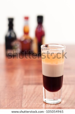 B 52 alcoholic drink layered in a tall shot glass with out of focus bottles in the back