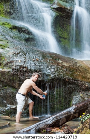 Young man drinking fresh clean water from a natural spring running down large rocks