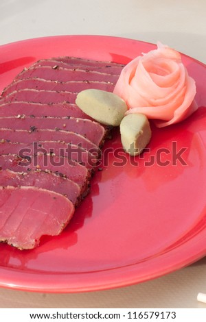 seared ahi tuna rare served on a red plate garnished with a pickled ginger rose and wasabi