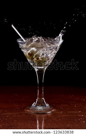 vodka martini isolated on a black background with olives splashing on a wet bar