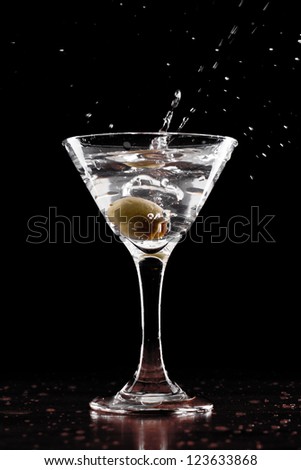 vodka martini isolated on a black background with an olive splashing and air bubbles