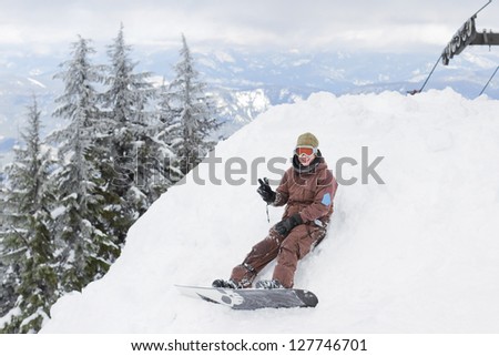 male snowboarder sitting down resting on a pile of snow