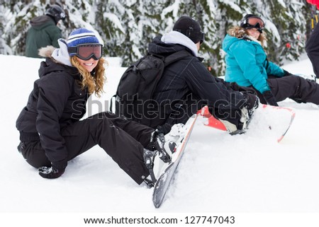 group of friends sitting on snow with snowboards and gear on and ready