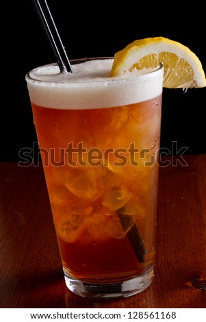 closeup of a long island red tea served on a dark bar top garnish with a lemon isolated on black