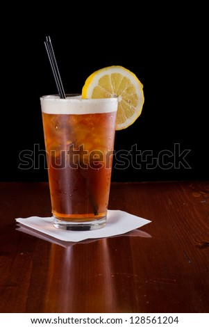 closeup of a long island red tea served on a dark bar top garnish with a lemon isolated on black