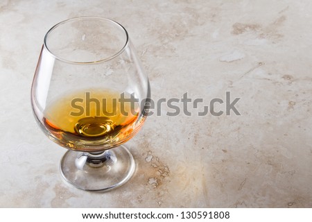 closeup of a brandy snifter on a marble table top with a golden reflection to the side